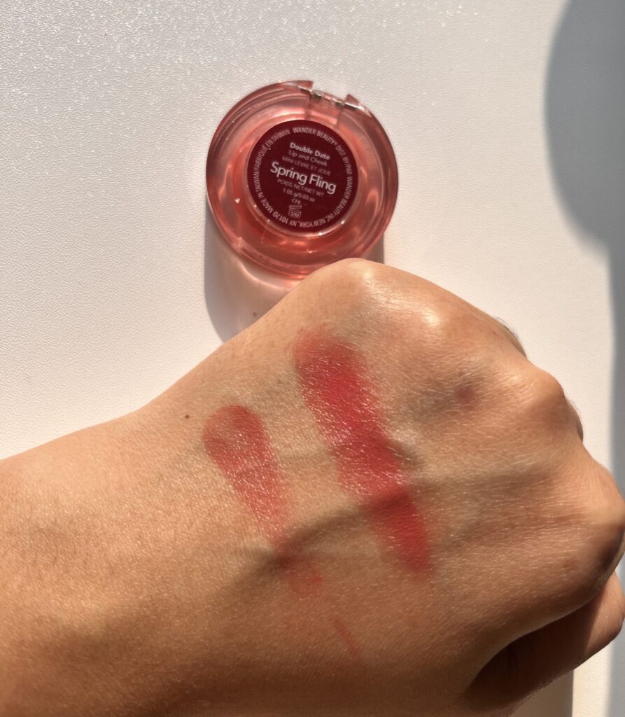 Hand swatch of Wander Beauty Double Date Lip and Cheek Spring Fling under natural sunlight, single swipe on left and multiple swipes on right