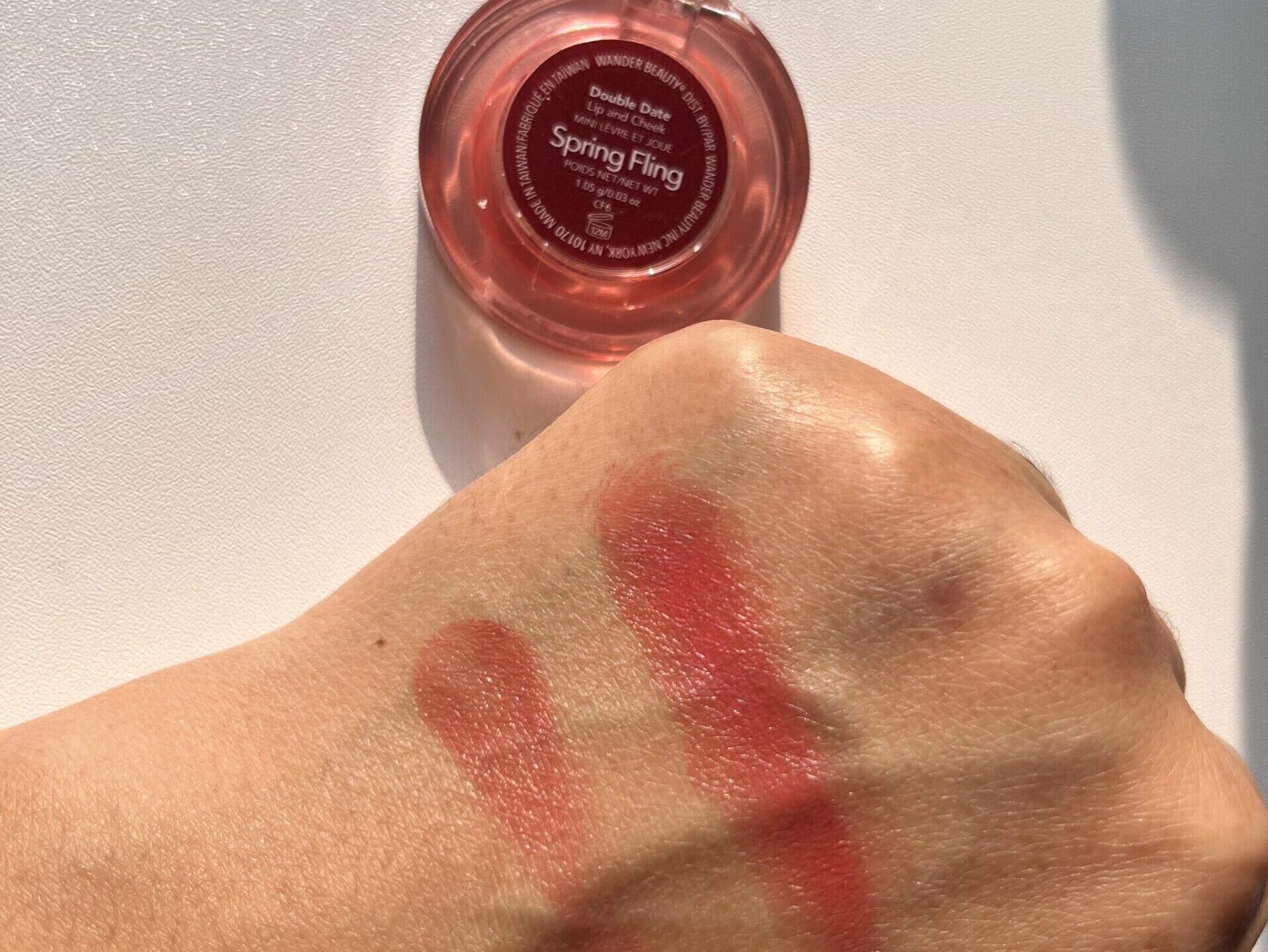 Hand swatch of Wander Beauty Double Date Lip and Cheek Spring Fling under natural sunlight, single swipe on left and multiple swipes on right