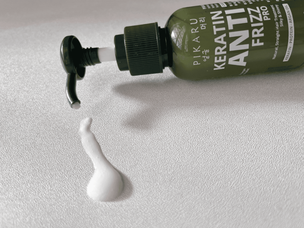 Pikaru Keratin Anti-Frizz Pro Hair Cream on a clean white background with a small amount of serum spilled beside the bottle.
