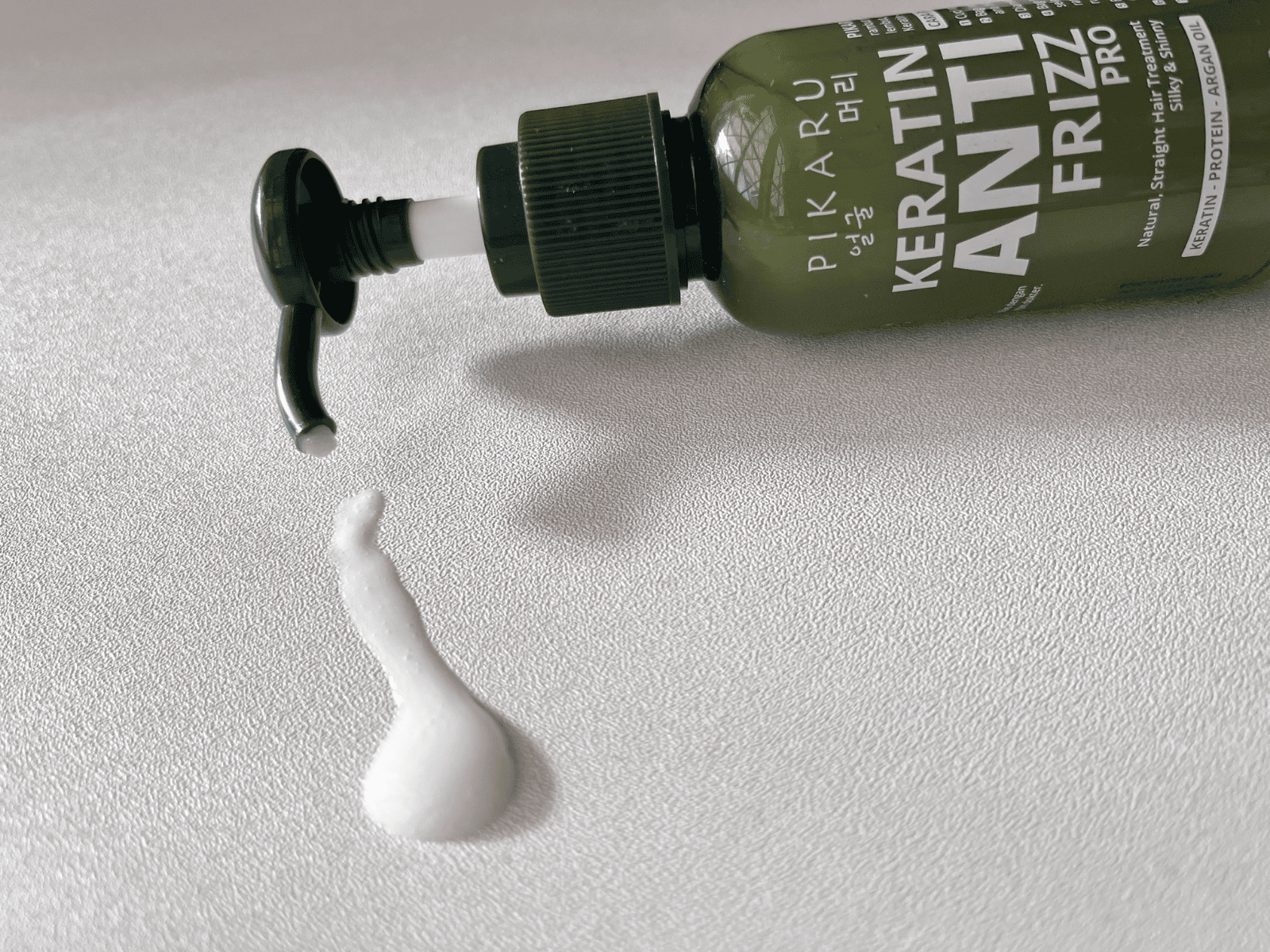 Pikaru Keratin Anti-Frizz Pro Hair Cream on a clean white background with a small amount of serum spilled beside the bottle.