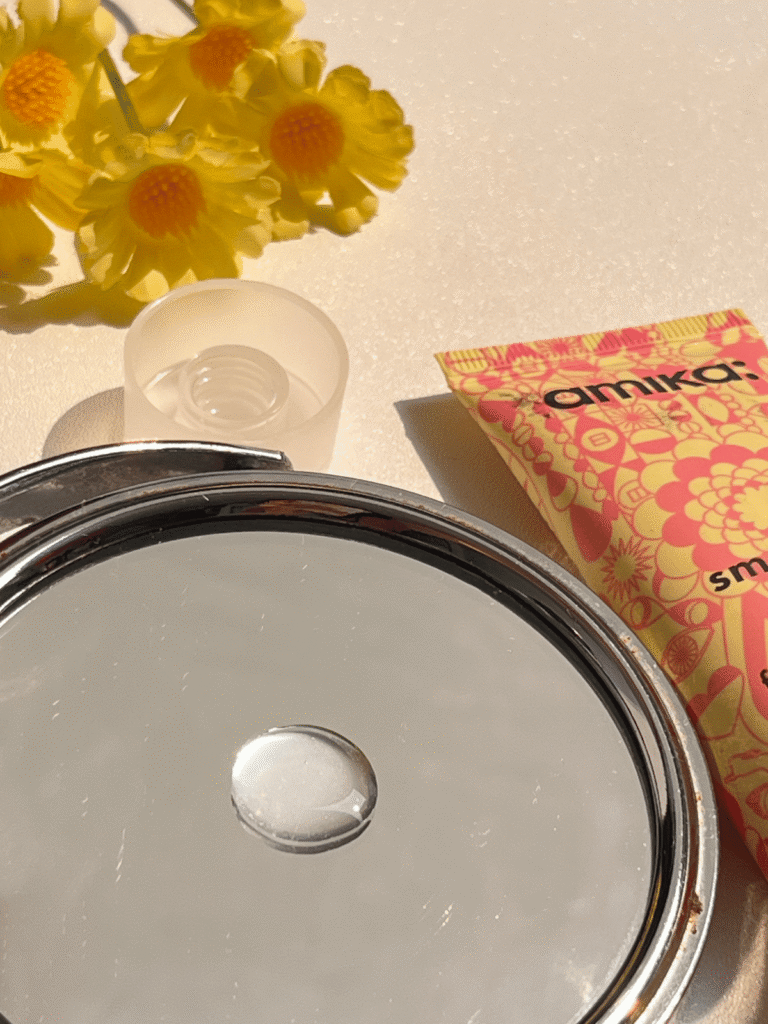 Texture of amika Smooth Over Frizz-Fighting Treatment with the product tube in the background
